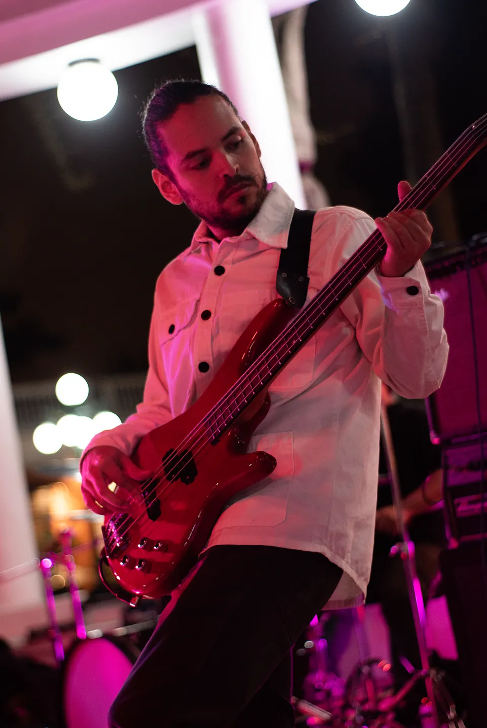 Bajista con camisa blanca y bajo rojo durante una presentación en vivo.